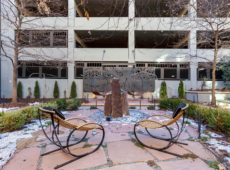 Courtyard Lounge with Stones, Contemporary Rocking Chairs and Contemporary  Round Swings in Front of Decorative Metal Piece in Front of Parking Garage